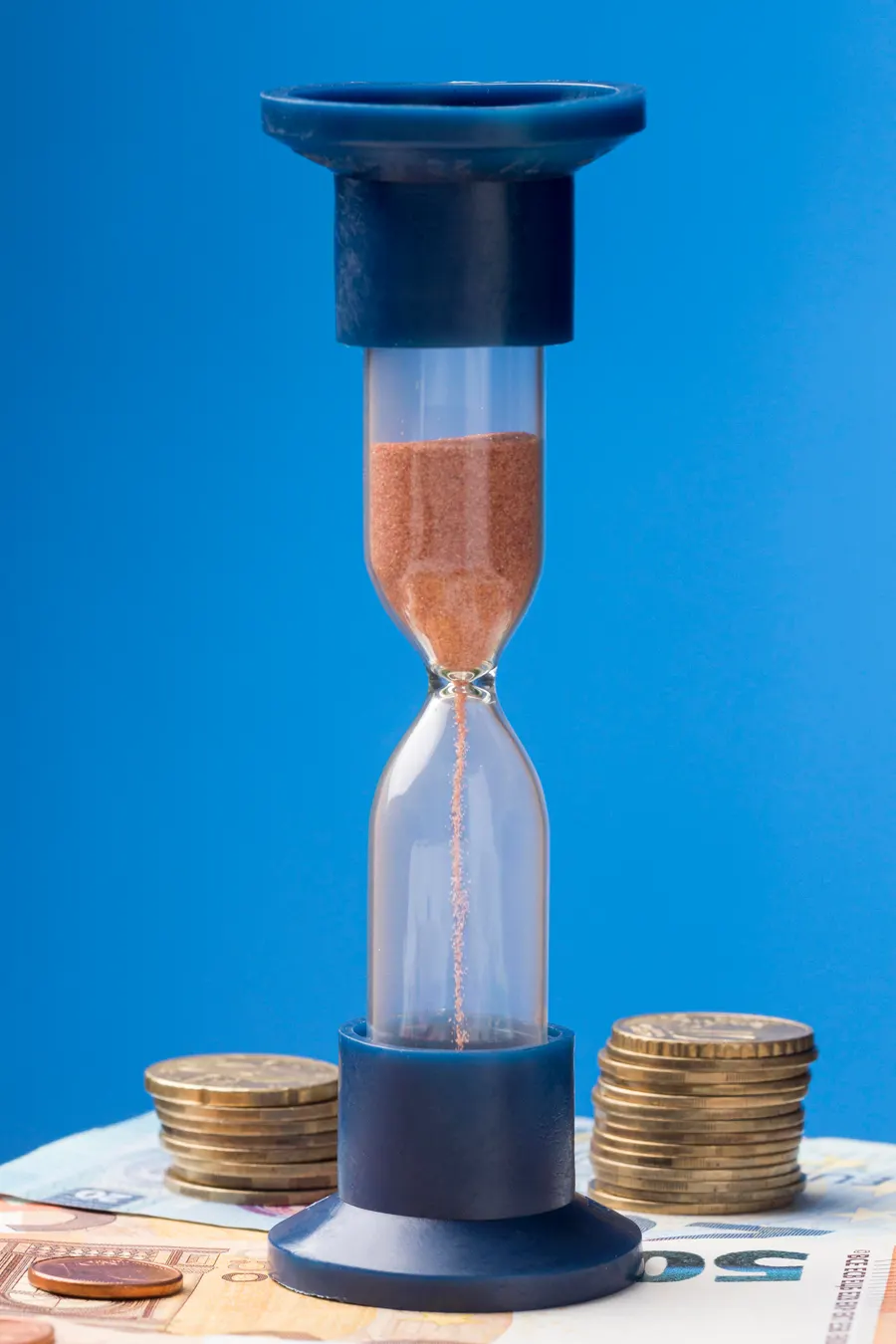 Timeglas omgivet af mønter viser at tid er penge, når man venter med at investere